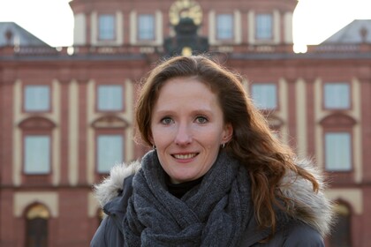 Prof. Hoisl has long brown hair and is standing in front of the castle.