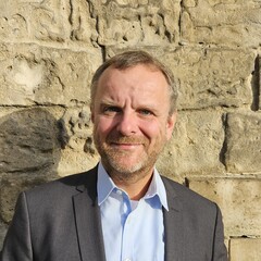 Prof. Ruenzi hat kurze Haare und trägt einen Anzug. Er steht vor einer Sandsteinmauer.
