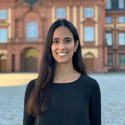 Raquel Oliveira hat lange braune Haare und trägt ein dunkles Oberteil. Im Hintergrund ist das Schloss zu sehen.