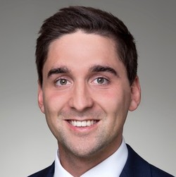 Christian hat kurze dunkle Haare und trägt ein weißes Hemd und einen dunklen Anzug.