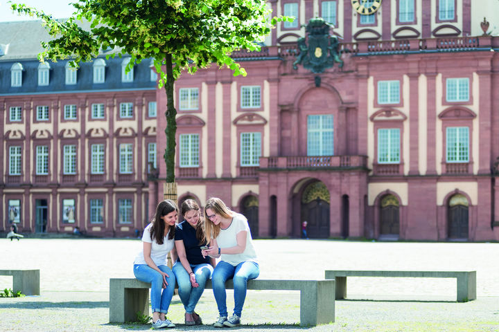 Studierende auf Bank vor dem Schloss