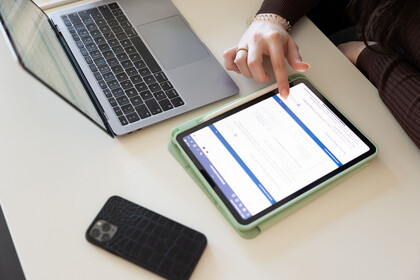 Eine Studentin tippt auf ihrem Tablet, ihr Handy und Laptop liegen daneben auf dem Tisch.