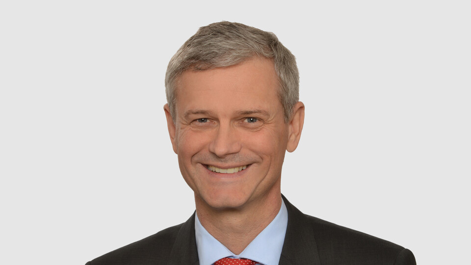 Prof. Helmig has short grey hair and wears a dark jacket, a light blue shirt and a red tie.