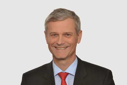 Prof. Helmig has short grey hair and wears a dark jacket, a light blue shirt and a red tie.