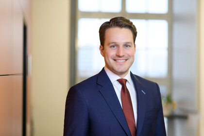 Prof. Glenk has short hair and wears a suit and tie.