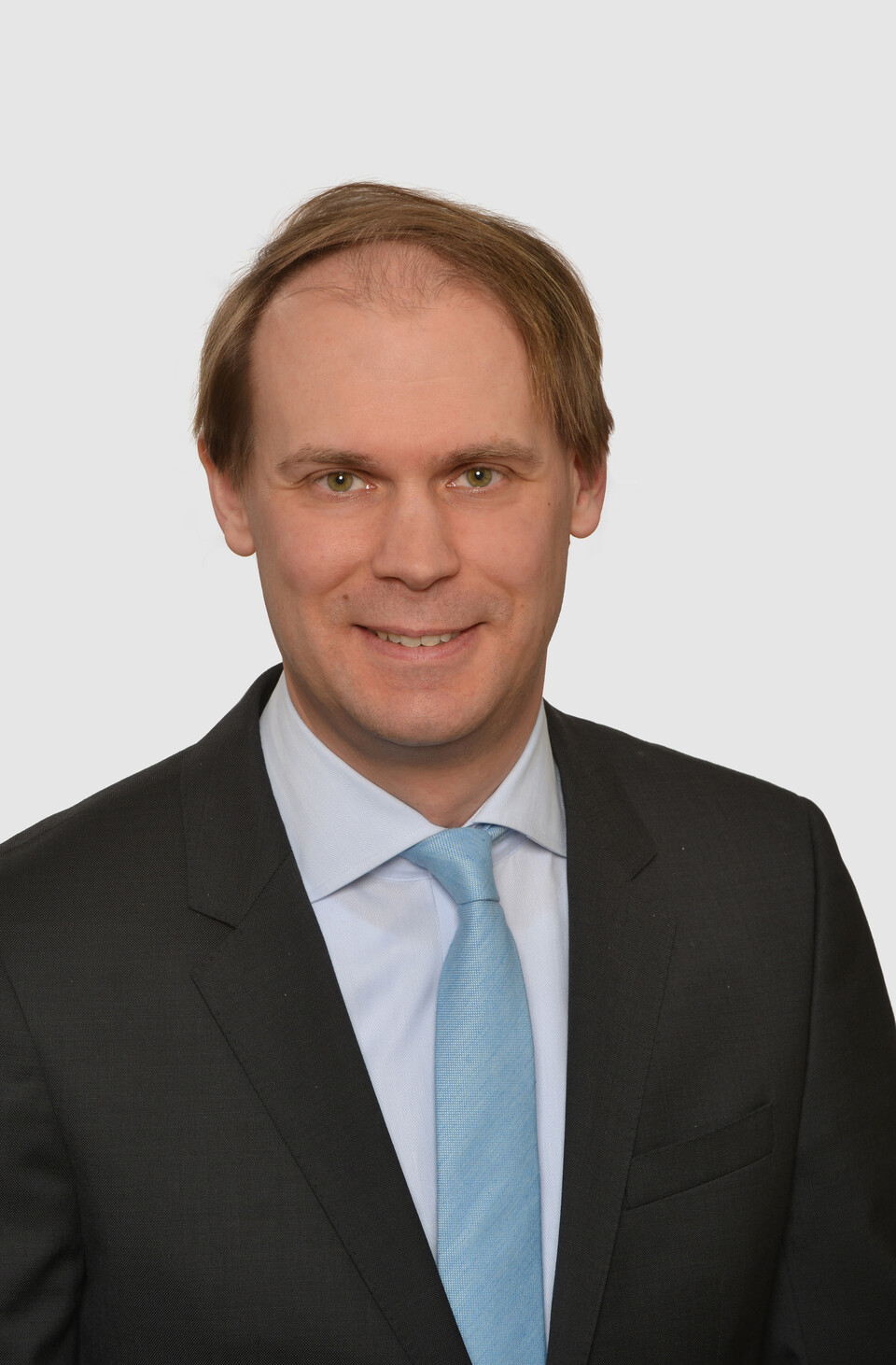 Prof. Bischof has short hair and wears a dark jacket, a light-colored shirt and a turquoise tie.