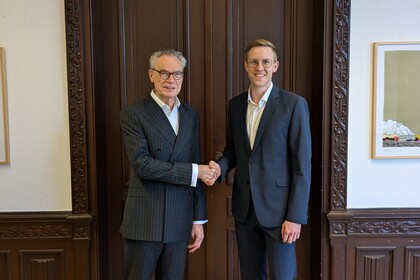 Dean Joachim Lutz and Prof. Dr. Jens Förderer stand in front of an ornate wooden door and shake hands