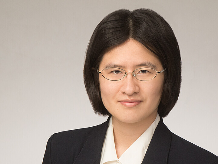 Yanghua Shi hat schwarze kinnlange Haare. Sie trägt eine feine Brille, einen dunklen Blazer und ein weißes Hemd.