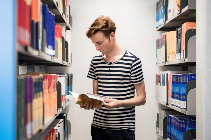 Student zwischen zwei Bücherregalen liest in einem Buch