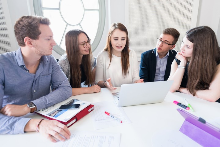 Students with laptops sit around a table